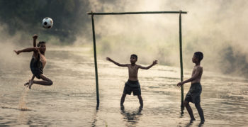 A young boy leaps out of water to perform a bicycle kick in game against two friends
